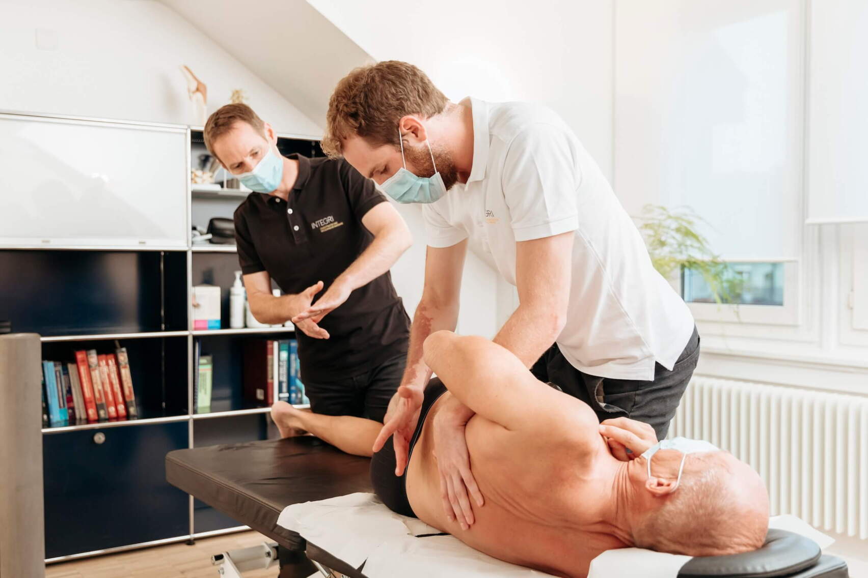 chiropraktik-behandlung-ruecken.jpg Zwei Chiropraktiker behandeln einen Patienten auf einer Behandlungsliege. Der Fokus liegt auf der Mobilisation der Wirbelsäule.